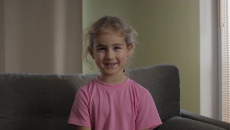 Kid-Child-Girl-Making-Online-Video-Call-Recording-Vlog-Sitting-On-Sofa-,-Portrait.-Funny-Girl-Smiling-Looking-At-Camera.-Happy-Cute-Little-Vlogger-Saying-Hello-Hi-Looking-At-Camera-Talking-To-Webcam.