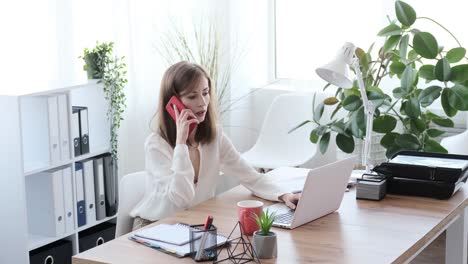 Businesswoman-talking-on-mobile-phone-while-working-on-office-laptop