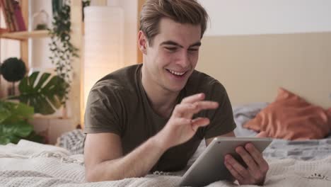 Happy-man-using-digital-tablet-in-bed