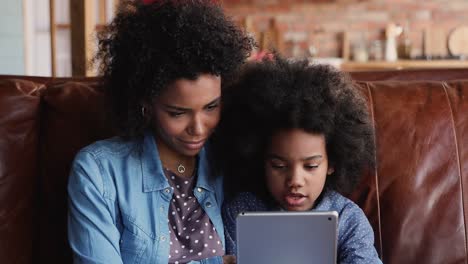 Madre-africana-educar-a-la-pequeña-hija-sosteniendo-tableta-utilizando-sitio-web-de-Internet