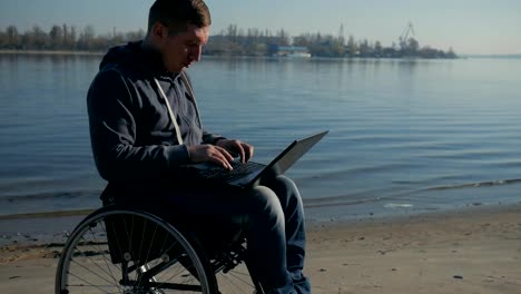 Disabled-man-in-wheelchair-works-on-laptop-by-the-river