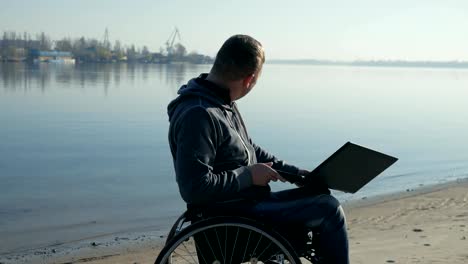 Disabled-person-in-wheelchair-with-laptop-leads-video-chat,-alone-by-the-water