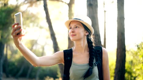 Funny-tourist-girl-in-hat-taking-selfie-photos-with-smartphone-camera-during-travelling-and-hitchhiking