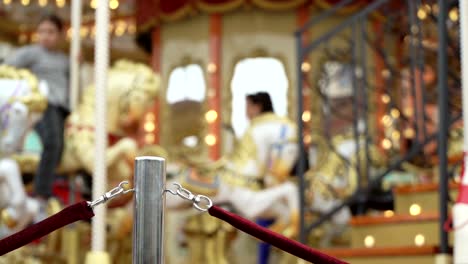 Merry-go-round-carousel.-Happy-kids-with-parents-riding-carousel-and-taking-pictures-and-selfies,-rope-fence-made-from-red-velvet,-employee-closes-door