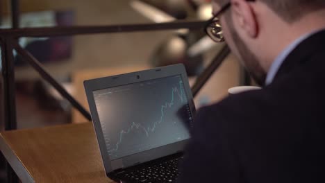 Young-man-monitors-trading-cryptocurrency-and-drinking-coffee-in-a-cafe