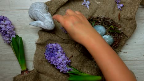 Hands-decorate-table-with-Easter-nest-with-colored-eggs-and-flowers