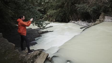 young-man-in-warm-clothes-takes-photos-on-mobile-phone-in-nature