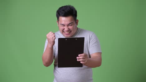 Young-handsome-overweight-Asian-man-against-green-background