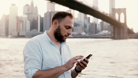 Serious-European-businessman-typing-message-on-smartphone-messenger-app-at-amazing-New-York-City-sunset-scenery-4K