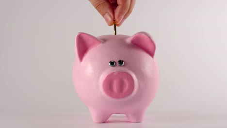 Male-hand-throws-metal-golden-coin-into-a-pink-piggy-moneybox