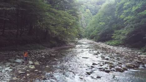 Mujer-caminando-por-la-orilla-del-río-con-aguas-color-turquesa-en-bosque-verde-zángano-vista