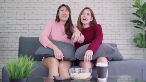 LGBT-lesbian-women-couple-moments-happiness.-Lesbian-women-couple-together-indoors-concept.-Friends-young-smiling-women-at-home-sitting-on-the-couch-and-watching-tv,-She-is-holding-a-remote-control.