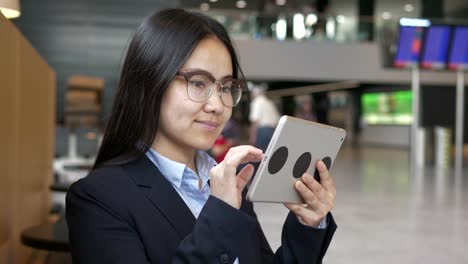 Mujer-bonita-joven-navegando-por-internet-con-tableta-digital-en-edificio-público