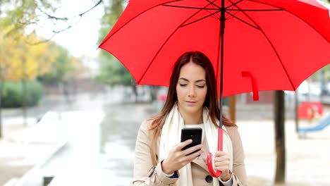 Serious-woman-checking-phone-under-the-rain