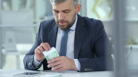 Businessman-Counting-Cash-with-Digital-Tablet