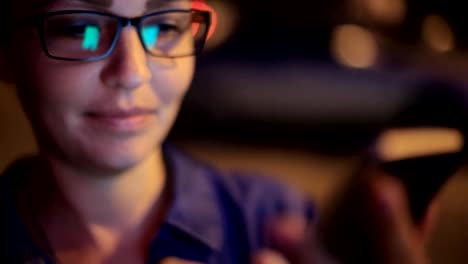 Retrato-de-la-joven-mujer-caucásica-hermosa-usando-la-mano-del-teléfono-inteligente-mantener-al-aire-libre-en-la-noche-de-la-ciudad,-sonriendo,-cara-iluminada-ScreenLight-red-social,-tecnología,-concepto-de-comunicación