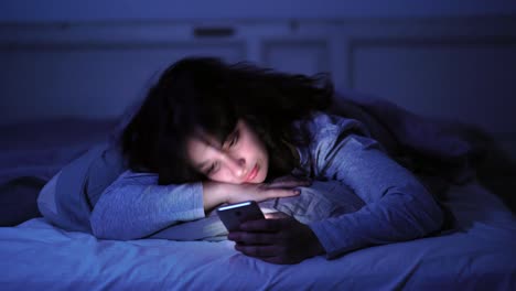 4K-wide-video-of-an-Addicted-young-woman-chatting-and-surfing-on-the-internet-using-her-smart-phone-sleepy,-bored-and-tired-late-at-night.-Dramatic-dark-light.-In-Internet,-Mobile-addiction-and-insomnia-concept.