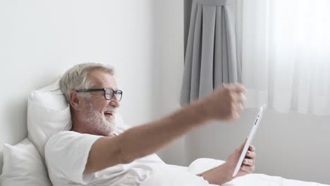 Grandfather-or-senior-man-using-tablet-technology-and-cheer-up-on-bed