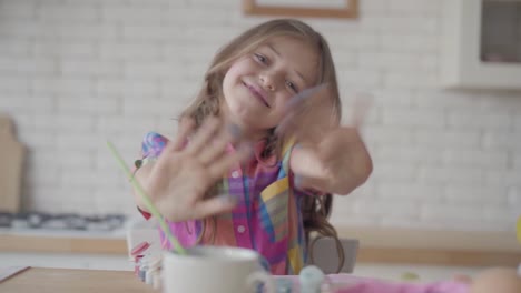 Portrait-funny-cute-emotional-little-girl-showing-hands-in-the-blue-paint