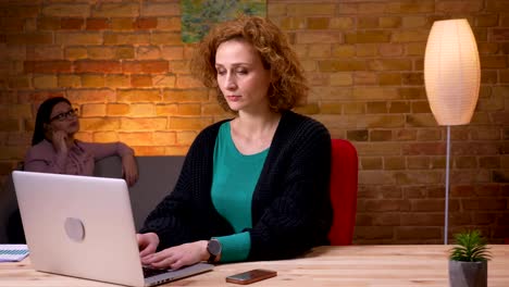 Closeup-shoot-of-young-businesswoman-working-on-the-laptop-having-a-phone-call-and-relaxing-indoors-in-the-office.-Female-employee-calling-on-the-cellphone-on-the-background