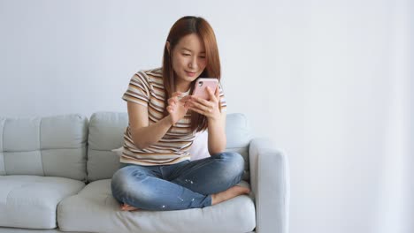 Mujer-asiática-usando-teléfono-celular-en-la-sala-de-estar