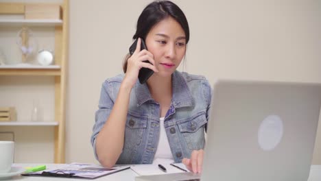 Beautiful-smart-business-Asian-woman-in-smart-casual-wear-working-on-laptop-and-talking-on-phone-while-sitting-on-table-in-creative-office.-Lifestyle-women-working-at-home-concept.