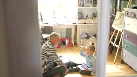 Grandpa-looks-photo-album-with-his-wedding,-little-boy-using-electronic-tablet