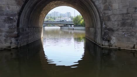 Flying-along-the-city-river-,-over-and-under-the-ancient-stone-bridge.