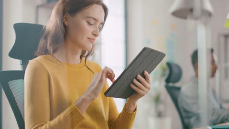 Talentierte-Designerin-sitzt-an-ihrem-Schreibtisch-und-verwendet-Touchscreen-Digital-Tablet-Computer.-Bright-Office,-in-dem-ein-vielfältiges-Team-junger-Berufstätiger-arbeitet