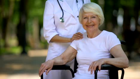 Doctor-poniendo-la-mano-en-el-hombro-de-la-anciana-discapacitada-mujer-mirando-a-la-cámara