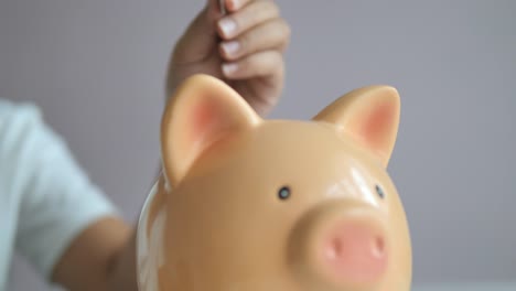 Close-up-hands-of-woman-putting-coin-into-the-piggy-bank-metaphor-saving-money-for-better-future-select-focus-shallow-depth-of-field