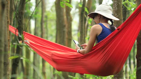 Mujer-relajándose-en-hamaca-con-teléfono-inteligente-en-la-selva-tropical,4k