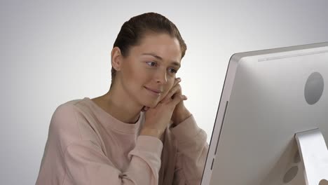 Blonde-girl-with-pink-pullover-looking-at-monitor-of-computer-watching-video-on-gradient-background