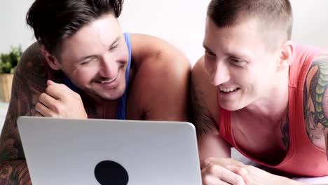 Gay-couple-in-bed-using-laptop-computer.-Focus-mood.