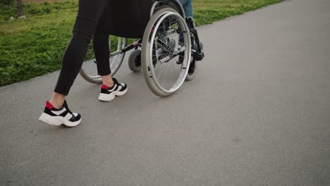 Woman-is-rolling-invalid-carriage-with-adult-man-outdoors,-close-up-of-legs