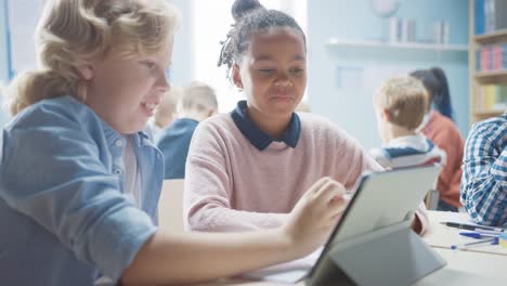 In-der-Grundschule:-Mädchen-und-jungen-Arbeiten-als-Team-mit-Tablet-Computer.-Vielfältiges-Klassenzimmer-mit-Kindern,-die-Programmiersprache-und-Softwaredesign-lernen