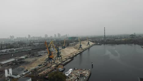 Baukräne-im-Industriepark-der-Stadt-bewegen-Sand-von-Binnenschiff-zu-Sand-Lkw.-Luftbild