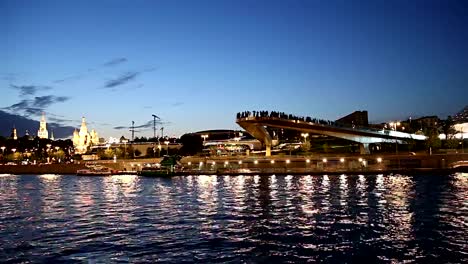 Schwimmende-Brücke-von-Zaryadye-Park-auf-Moskvoretskaya-Embankment-des-Flusses-Moskva-(und-touristisches-Vergnügungsboot)-bei-Nacht.-Moskau,-Russland.