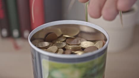 Männliche-Hand-gießt-Euro-Münzen-in-ein-Glas