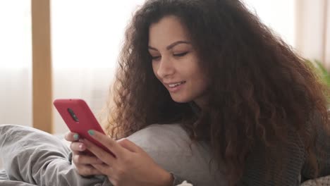 Smiling-woman-using-mobile-phone-in-bed