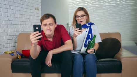 Happy-woman-sport-fan-winning-a-betting-and-watching-a-smartphone.-Disappointed-man-sport-fan-frustrated-by-losing-a-team.-Concept-of:-sports,-betting.-Bet-with-a-gambling-mobile-app.-Soccer-bet