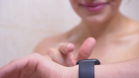 Attractive-young-woman-athlete-wearing-and-using-smartwatch-in-bathroom.-Taping-smartwatch-device-screen.