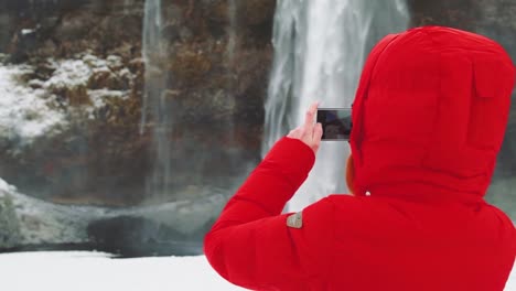 hermosa-joven-cerca-de-una-cascada-en-hielo,-toma-fotos-en-el-teléfono