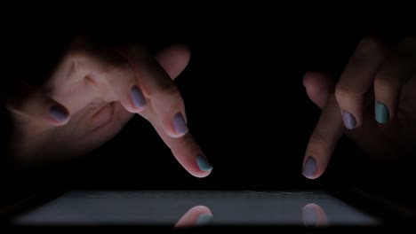 Close-up-hands-of-a-young-woman-in-a-dark-room-to-typing-text-on-the-touchscreen-of-the-tablet