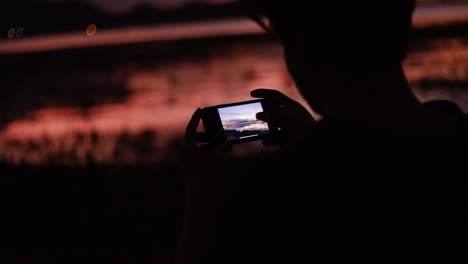 Silhouette-von-Nahaufnahme-asiatischen-Mann-mit-Smartphone-überprüfen-ein-Foto-nach-dem-Fotografieren-am-Meer-Strand-schönen-Sommer-Sonnenuntergang,-goldene-Stunde-Licht.