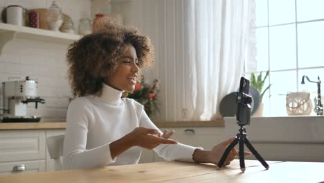 Glückliche-dunkelhäutige-Dame-sitzt-am-Tisch-und-schießt-Video-Blog