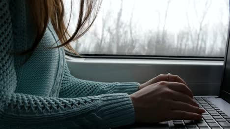 Female-hands-typing-on-keyboard-of-laptop-in-train.-Woman-chatting-with-friends-during-traveling-on-railway.-Young-girl-using-notebook.-Arm-print-a-message.-Close-up