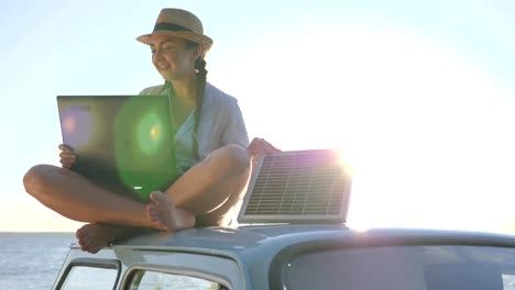 new-technology,-happy-girl-sits-on-roof-classic-car-with-solar-battery-and-laptop-in-hands-in-open-air,-female-sitting-on-car