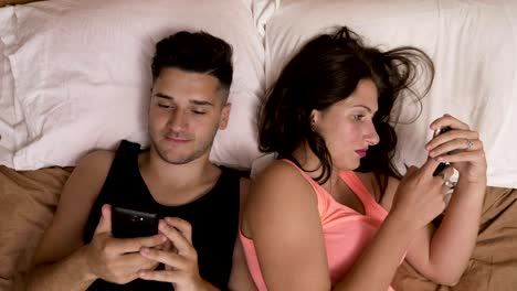 Young-couple-laying-in-bed-chatting-on-social-media-addicted-to-smartphones-ignoring-each-other