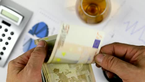 Man-counting-european-paper-money,-euros-on-the-background-of-a-diagram-and-a-cigar